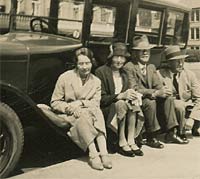 Two women and two men sat on a car's running board