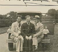 Three men sat on the front of a vintage car