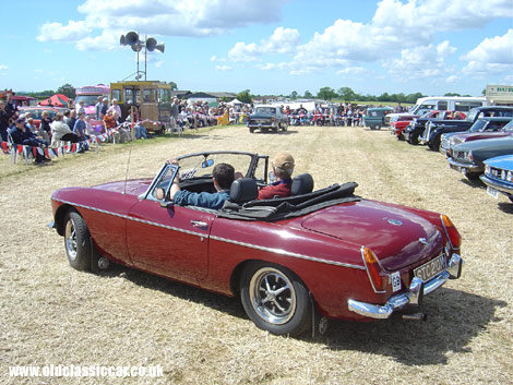 An MGB Roadster drives around a display arena at a show.